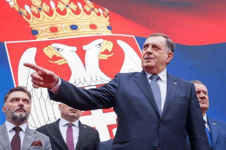 Bosnian Serb leader Milorad Dodik gestures while speaking in front of a large Serbian coat-of-arms backdrop.