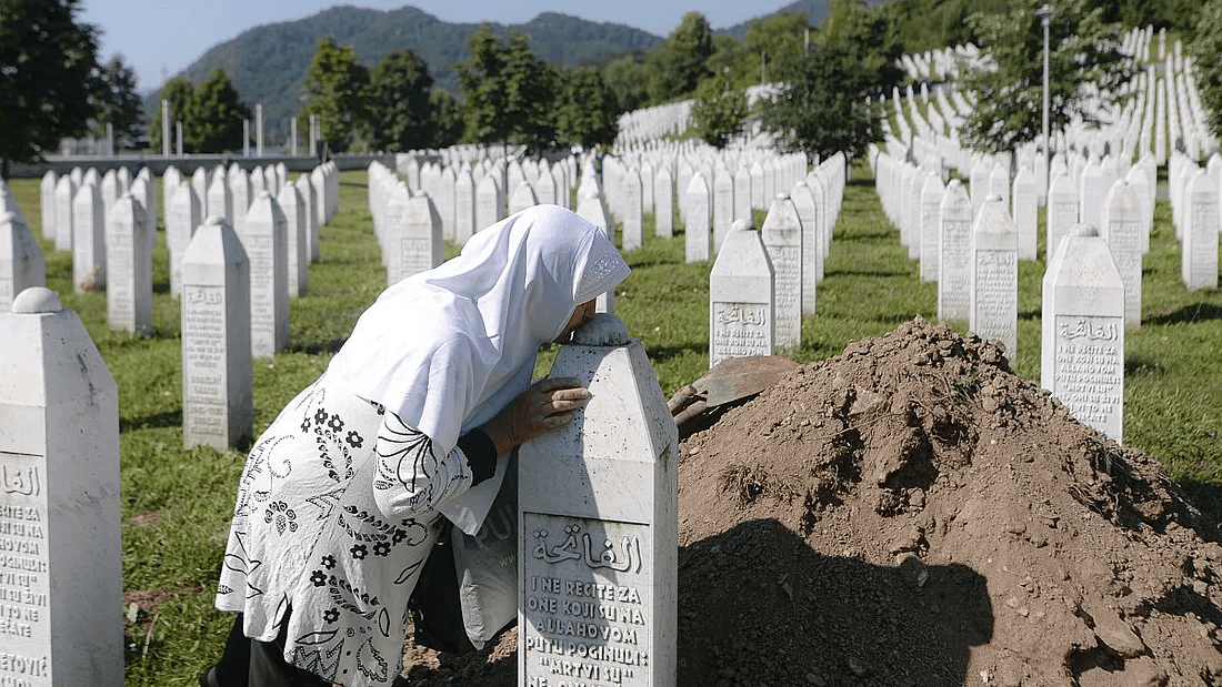 A woman in a white headscarf rests her head against a white gravestone at the Srebrenica-Potočari Memorial Center.