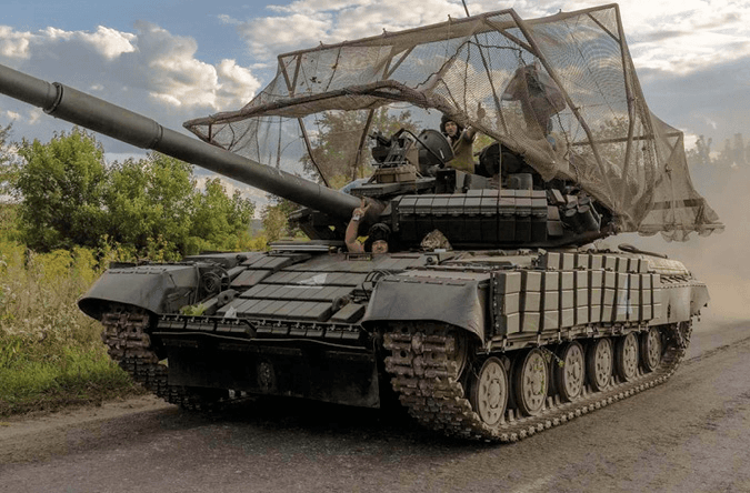 A tank fitted with anti-drone netting drives along a road in Ukraine.
